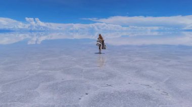 Bolivya 'daki geniş Salar de Uyuni tuz düzlüklerinde koşan bir kadın, açık mavi gökyüzünün altındaki dünyanın en büyük tuzlu dairesinin dingin güzelliğini yakalıyor..