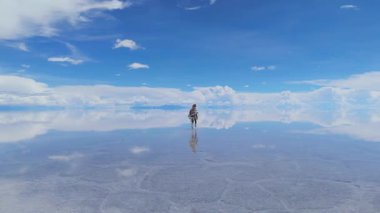 Bolivya 'daki geniş Salar de Uyuni' de bir kadın koşuyor, yansıması kristal berrak sularda parlak mavi bir gökyüzünün altında yansıyor..