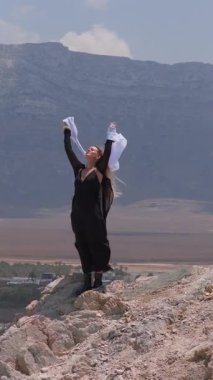 Siyah elbiseli bir kadın, Socotra, Yemen 'de denize bakan kayalık bir uçurumda duruyor. Beyaz atkısı rüzgarda dalgalanır..