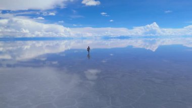 Bolivya 'daki geniş Salar de Uyuni tuz düzlüklerinde, berrak mavi bir gökyüzünün altında tek bir kişi dolaşır..