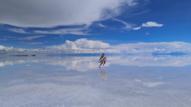 Bir kadın, Bolivya 'daki geniş Salar de Uyuni tuz düzlüklerinde koşuyor. Vücudu kristal berrak suda kusursuz bir şekilde yansıyor..