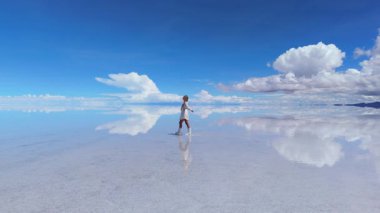 Bolivya 'daki geniş Salar de Uyuni' de yürüyen bir kadın, yansıması kristal berrak sularda parlak mavi bir gökyüzünün altında yansıyor..