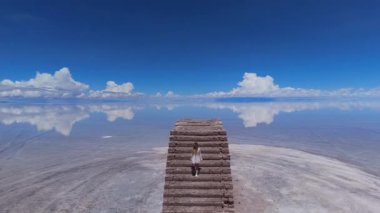 Genç bir kız, açık mavi gökyüzünün altında, Bolivya 'daki Salar de Uyuni tuz düzlüklerinin uçsuz bucaksız genişliğini keşfeder..