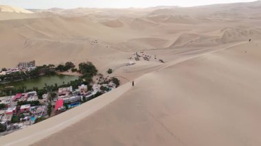 Peru 'daki Huacachina vahasının havadan görünüşü, kum tepeleri ve sakin bir göl sergileniyor..
