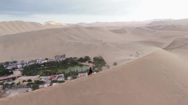 Uçsuz bucaksız kum tepelerinin arasına yerleşmiş, dingin bir göl ve yemyeşil bir yeşilliğe sahip bir Peru kasabasının havadan görünüşü..