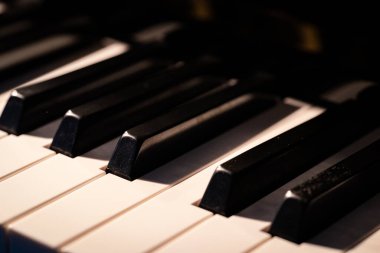 Sıcak ışık altında piyano tuşlarının yakın görüntüsü, siyah ve beyaz tuşların zarif kontrastını gösteriyor. Müzik, sanat, yaratıcılık ve klasik enstrüman kavramları için ideal.