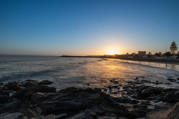 Altın gün batımı, Gran Canaria 'daki kumlu bir sahilde sakin okyanus dalgalarını yansıtıyor. Yürüyen ve yüzen insanlar rahatlatıcı, tropikal bir tatil ortamı yaratırlar..