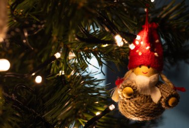 Sıcak peri ışıklarıyla süslenmiş bir ağaca asılı el yapımı Noel cücesi süsü, rahat ve şenlikli bir tatil atmosferi yaratıyor..