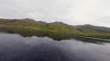 Alaska 'nın yeşil kıyı şeridini ve dağ yamaçlarını gören dinamik bir uçuş. Unalaska adası, sessiz körfezin havadan görünüşü ve doğal güzellik. Hollanda Limanı, Aleutians Adaları, Alaska.