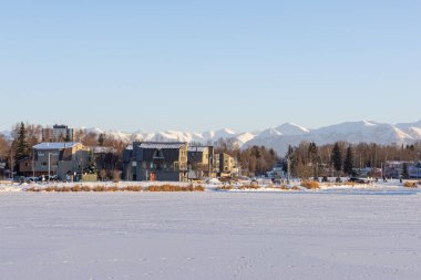 Geniş Alaska Dağları ile Anchorage Evleri. Soğuk arazi ve görkemli beyaz dağ sırtlarıyla çevrili bir Anchorage mahallesinin huzurlu kış manzarası. Alaska şehri.