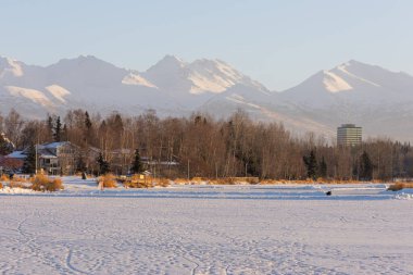 Anchorage Alaska 'nın Kış Şehri manzarası, donmuş bir şehir gölü ve karla kaplı dağları ile Amerikan şehrini çevreleyen. 
