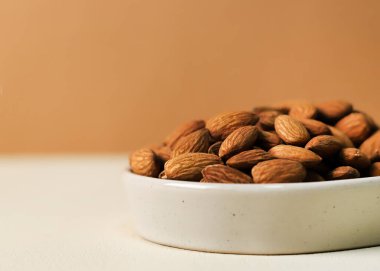 Tarafsız bir zeminde beyaz bir seramik kasede kavrulmuş badem.