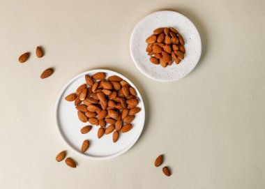 Beyaz seramik tabakalardaki tüm ham bademlerin bej arkaplan üzerindeki üst görünümü