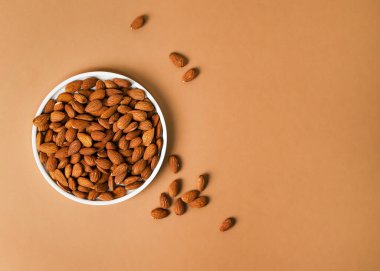 Beyaz benekli seramik tabakta kavrulmuş bademlerin bej arkaplanda fotokopi alanı ile üst görünümü