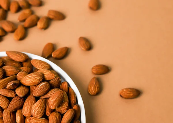 Beyaz benekli tabakta kavrulmuş badem fıstıklarının üst görünümü ve bej arkaplanda kopya alanı