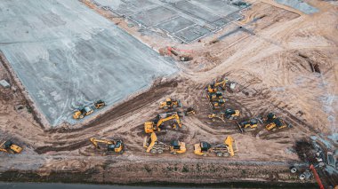 Ağır makineler, kazıcılar, buldozerler, çöp kamyonları ve arazi geliştirme ve inşa vakfı üzerine çalışan diğer ekipmanların bulunduğu inşaat alanının havadan görüntüsü.