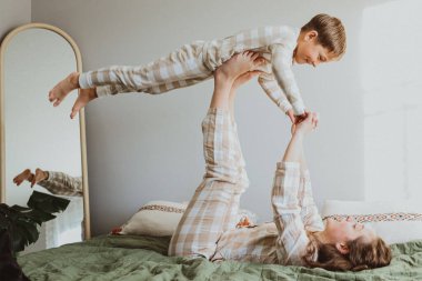 Kız kardeşi erkek kardeşiyle yatakta uçak oyunu oynuyor. Evde rahat pijamalarıyla eğlenceli ve eğlenceli bir aile anı yaşıyor. Yüksek kalite fotoğraf