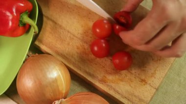 Tahtada kırmızı kiraz domateslerini ikiye bölerek sulu dokuyu ve tazeliği ortaya çıkarıyor. Domatesler soğan ve biberin yanında parlar. Ev yemeği ve sağlıklı yemek kavramı.