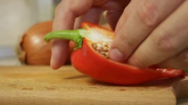 Erkek elleri, soğan ve domatesle ahşap kesme tahtasındaki olgun kırmızı dolma biberi temizler. Parlak sebzeler canlı kontrast gösteriyor. Yemek tasarımı, yemek pişirme kontrastı ve mutfak hazırlığı kavramı