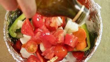 Folyo kaplı tabakta renkli sebzelerin üzerine zeytinyağı serpiştirilmiş. Dolmalık biber, domates, soğan ve havuç parlatıcı ve kontrastı yansıtır. Görsel içerik için gıda tasarımı ve mutfak sunumu sahnesi.