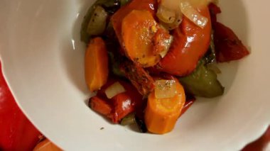 Kavrulmuş sebzeler tabakta dinleniyor, dokuyu ve kontrastı sıcak tonlarda gösteriyor. Soğan ve biberle çevrili sebze renkleri, kırsal ahenk yaratır. Sebze kavramı birleşim ritüeli olarak.