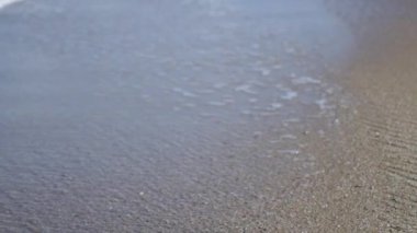 Köpüklü deniz dalgaları kumlu sahile dökülüyor. Yakın plan. Yüksek kaliteli FullHD görüntüler