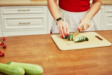 Genç kadın evdeki mutfakta sebze ve meyve kesiyor. Mutfak masasında taze meyve ve sebze var. Yemek pişirmek için malzemeler. Kapat.