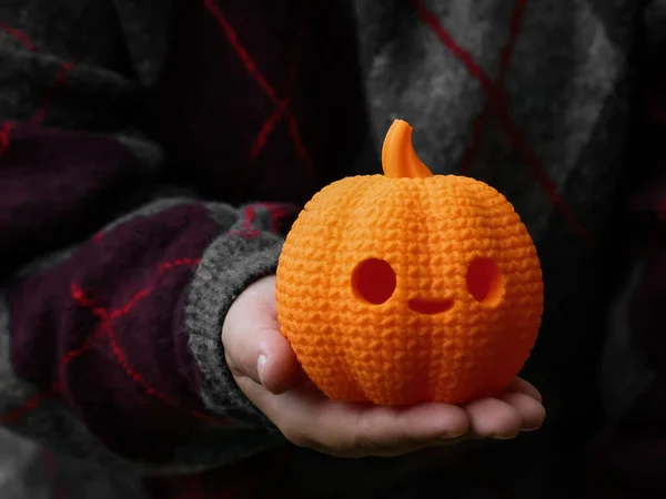 Hoş bir sonbahar sahnesi. İçinde gülen yüzlü, turuncu bir balkabağı süslemesi var. Bir insanın elinde. Sıcak süveter mevsimlik çekiciliğe katkı yapıyor, sonbahar havası için mükemmel oluyor..