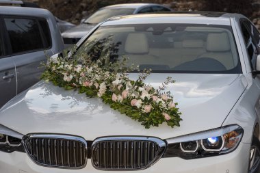 Çiçek aranjmanlı bir arabanın düğün süslemesi, kaputunda düğün çiçekleri olan beyaz bir araba.