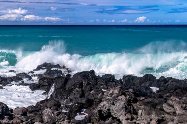 Büyük Hawaii Adası 'nın batı kıyısında okyanus dalgaları kıyıya vuruyor. Arka planda bulutlu mavi gökyüzü ve Pasifik Okyanusu.