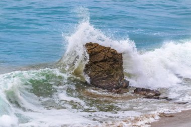 California, Malibu 'da Leo Carrillo sahilinde dalgalar kayalara çarpıyor. Sprey havaya uçuyor. Arka planda Mavi Pasifik Okyanusu.