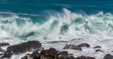 Büyük Hawaii Adası 'nın batı Kona kıyısındaki kayalıklara çarpan dalgaların panoramik görüntüsü. Köpük, ön planda volkanik kayalar. Arka planda turkuaz Pasifik Okyanusu.