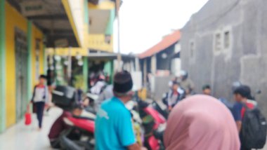 Bulanık, yumuşak odaklı bir fotoğraf bir grup öğrenciyi sırt çantasıyla bir okul binasının önünde dikilirken ve yürürken çekiyor..