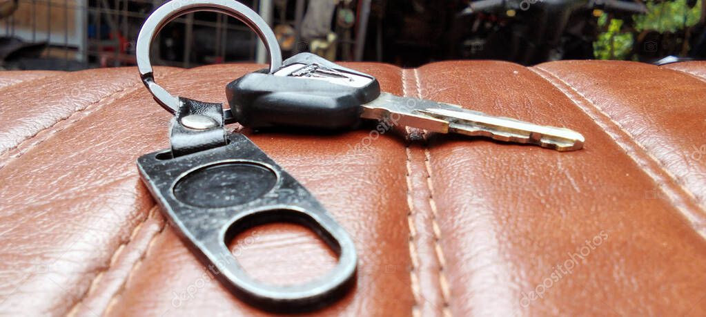 The motorcycle key is placed on the brown leather seat with clearly visible stitching.