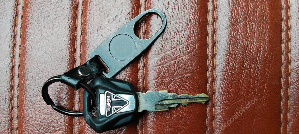 The motorcycle key is placed on the brown leather seat with clearly visible stitching.