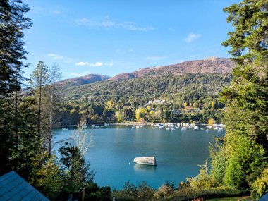 Kuzey Patagonya 'daki Nahuel Huapi Gölü' nün sakin sularına bakan, Villa La Angostura 'daki Puerto Manzano' nun sonbahar manzarası. Küçük tekneler, yoğun Andean-Patagonya ormanları ve dökülen yapraklarla çevrili turkuaz göl üzerinde huzur içinde dinleniyor..