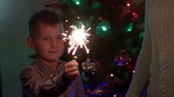 Madre y su hijo sonriendo y mirando los destellos del fuego de bengala en Navidad — Vídeo de stock