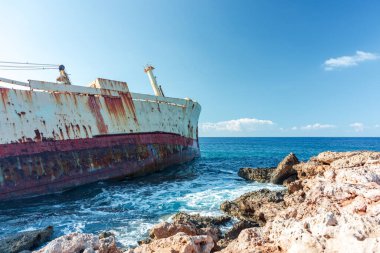 Turkuaz dalgalar kıyıları yıkarken devasa, paslı bir Edro III gemisi sivri kayalara dayanır. Güneşli gökyüzü ve uzak bir ufuk çarpıcı bir çürüme ve okyanus sükuneti manzarası yaratır..