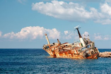 Paslı, terk edilmiş Edro III gemi enkazı, Kıbrıs, Pegeia, berrak mavi sularda kayalık bir dalgakırana yaslanıyor. Sahne deniz bozunmasını, dayanıklılığı ve yalnızlığı çağrıştırıyor. Geminin etrafında parlak bulutlar ve sakin bir deniz var..