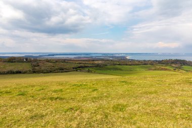 Swanage. Ballard Cliff yolu. Dorset. Uçsuz bucaksız yeşil tepeler ve açık alanlar parçalı bulutlu bir gökyüzünün altında uzak bir kıyı şeridine götürür. Huzurlu bir kırsal alan yaratır. Seyahat, doğa ya da yaşam tarzı temaları için mükemmel..