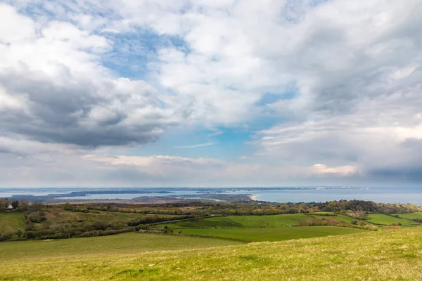 Swanage. Ballard Cliff yolu, Dorset. Yeşil tarlaları ve yuvarlanan tepeleriyle huzurlu bir kıyı manzarası dramatik, bulutlarla dolu bir gökyüzünün altında gözden kayboluyor..