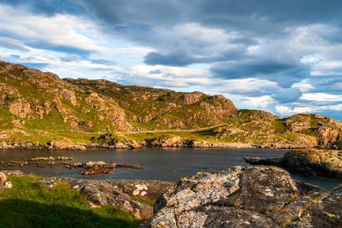 İskoçya İskoçya - Oldhoremore - Yeşil tepeler ve kayalık kıyı şeritleriyle engebeli bir kıyı sahnesi dramatik, bulutlarla dolu bir gökyüzü altında sakin sularla buluşuyor. Doğal güzellik ve açık hava sükuneti, deniz tarafından keşif ve yansımaya davetiye çıkarır.