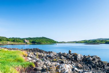 Kayalık bir kıyı şeridi, sakin bir Loch Dunvegan, uzak bir Dunvegan Kalesi, yelkenli, yemyeşil tepeler ve sahil boyunca bir kale harabesi. Seyahat, doğa ve açık hava yaşam tarzı kullanımı için ideal.