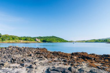 Kayalık bir kıyı şeridi, sakin bir Loch Dunvegan, uzak bir Dunvegan Kalesi, yelkenli, yemyeşil tepeler ve sahil boyunca bir kale harabesi. Seyahat, doğa ve açık hava yaşam tarzı kullanımı için ideal.