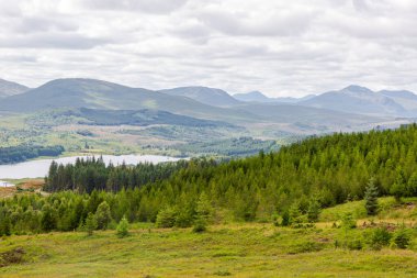 İskoçya 'nın Skye adası- sakin ormanlık tepeler, sakin bir göl ve yumuşak, bulutlu bir gökyüzünün altındaki uzak dağlar. Doğa, seyahat ve açık hava yaşam tarzı için ideal..