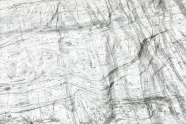 Gri damarlı ve pürüzsüz mermeri andıran kıvrımlı dokuların yer aldığı beyaz buz yüzeyinin detaylı bir yakın çekimi. Kış temaları, soğuk, jeoloji ve doğal desenler için ideal.