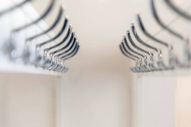 Metalik askıların beyaz çubuklar boyunca dizildiği, modern iç tasarımı ve düzenli depolama çözümlerini vurgulayan simetrik ve düzenli bir görünüm yaratan temiz, minimalist bir dolap sahnesi. Yaklaş, seçici odaklanma.