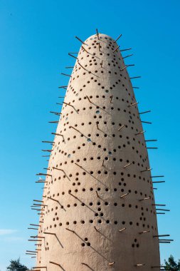Katara Kültür Köyü 'ndeki çarpıcı bir açık güvercin kulesi. Açık mavi gökyüzünde sayısız delik ve çıkıntılı çubuklar var. Doku, desen ve geometrik formu vurgulayan soyut, modern sanat.
