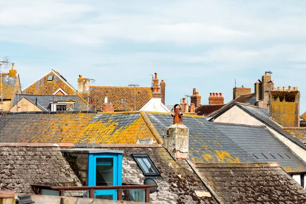 Mavi gökyüzünün altında sarı liken benekli bir sıra eski kayrak çatı. Mavi pencere çerçevesi ilginç bir şehir sahnesine renk katıyor, tarihi, havayı ve günlük yaşamı çağrıştırıyor.