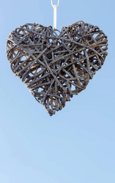 Birbirine dolanmış dallardan yapılmış el yapımı bir kalp, berrak mavi bir gökyüzüne asılı duruyor, pürüzsüz dokusu aşka dayandığını ve yavaşça kendini yeniden inşa ettiğini ima ediyor. Arkasındaki açık gökyüzü sessiz bir yenilenme hissi uyandırıyor.